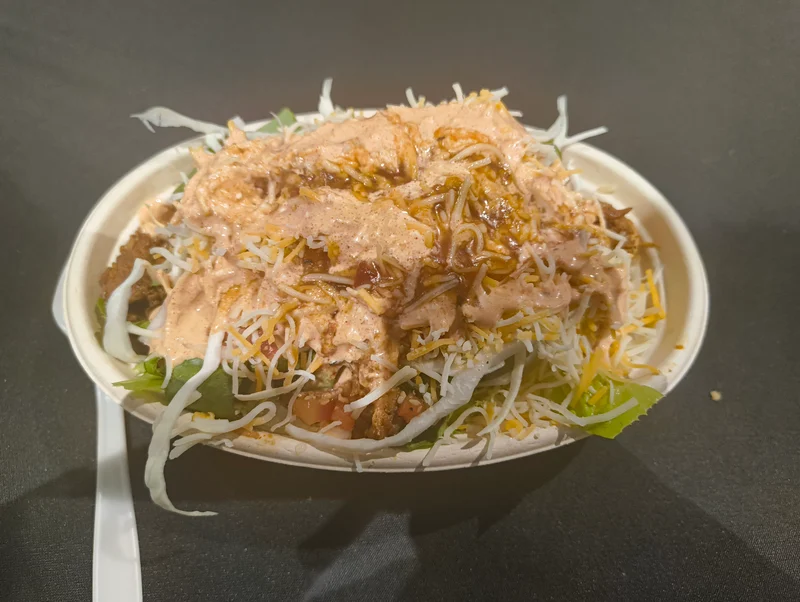 SC24会場のライスボウル。紙製の皿の上に入っており、細いチーズとキャベツで米が見えない。赤色のソースがかかっている